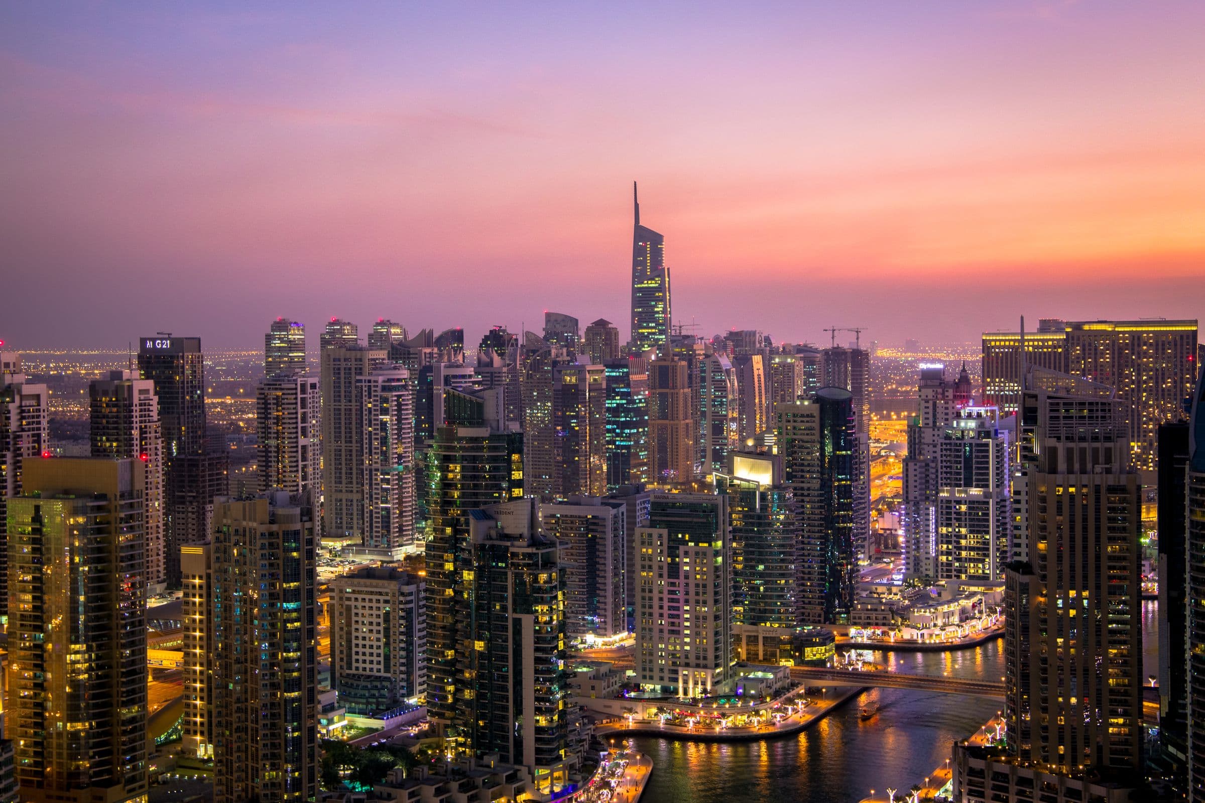 Dubai Marina towers lit up at dusk under a pink sky
